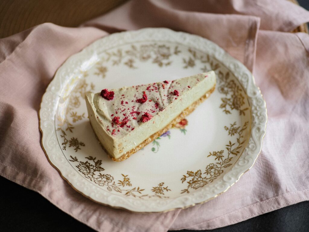 Aesthetic slice of raspberry cheesecake on a decorative plate with floral designs, ideal for food photography.