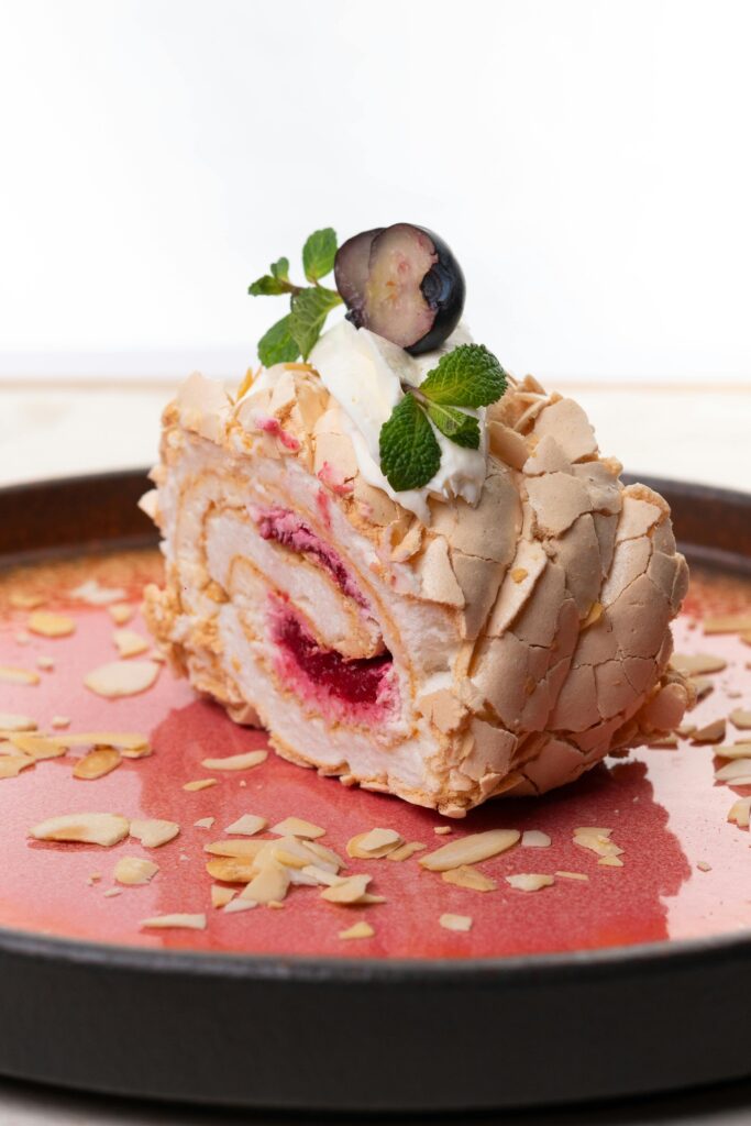 Close-up of a delectable berry meringue roll topped with cream and mint leaves.