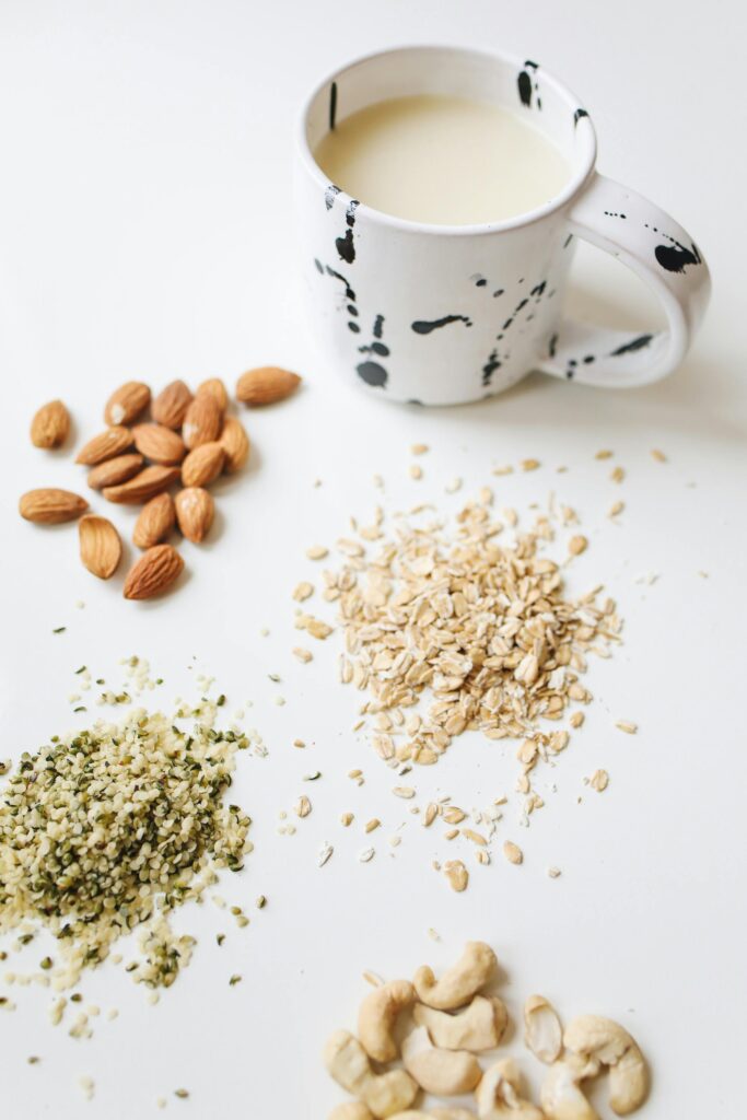 Overhead view of almonds, oats, hemp seeds, cashews, and milk in a modern mug on white surface.
